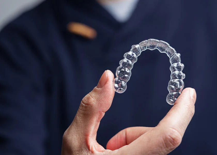 Hand hält eine transparente, herausnehmbare Zahnschiene vor dunklem Hintergrund